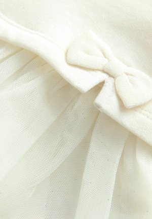  cremefarbener Kleidungsdetail mit einem weichen Stoff und einer Tüllüberlage, die einen kleinen Schleifenakzent in der Nähe des Ausschnitts aufweist.