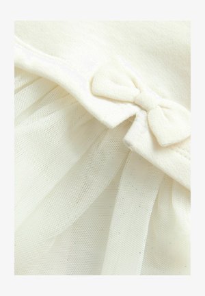 Szczegół w odzieży o kolorze kremowym, z miękkiego materiału i tiulowym nakładką, z małą kokardą w okolicach dekoltu.