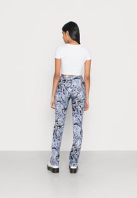 Calças com padrão marmoreado em azul e preto, com um design ajustado, feitas de um tecido suave. Compridas até aos tornozelos, com uma ligeira abertura na bainha.