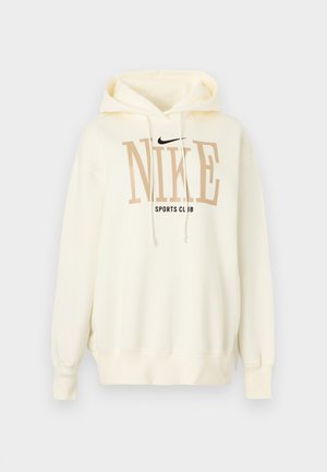 Μπεζ φούτερ Nike με κουκούλα, με κορδόνια μπροστά, μεγάλο μπεζ κείμενο "NIKE", μικρότερο μαύρο κείμενο "SPORTS CLUB" και μαύρο λογότυπο Nike swoosh.