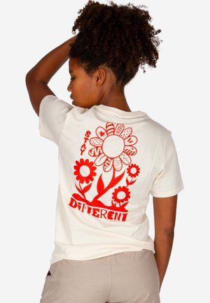 Woman with curly hair wearing a white T-shirt with red flower designs and the text "Stay Different" on the back.