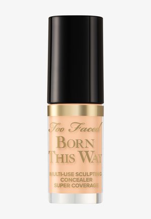 Too Faced Born This Way Multi-Use Sculpting Concealer-Flasche mit schwarzem Deckel und goldener Beschriftung auf hellbeigem Produkt.