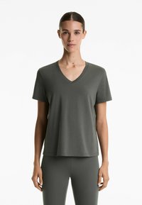 Tricou din bumbac verde închis, cu decolteu în V, mâneci scurte și o croială lejeră, asortat cu colanți corespunzători. Textură netedă, design minimalist.