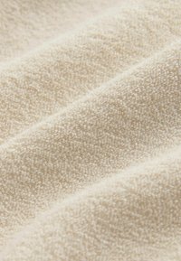 Beige strukturiertem Stoff mit einer weichen, flauschigen Oberfläche, die ein dezentes Gewebemuster und sanfte Falten aufweist, was eine taktile Erscheinung schafft.