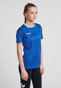 Blå kortärmad sporttröja med vit krage och svarta axeldetaljer. Har en mjuk textur och ett ventilerande material, logotyp synlig.