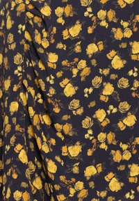 Tejido floral con rosas amarillas y acentos verdes sobre un fondo azul marino oscuro. Textura suave con caída ligera y logotipo de la marca visible.