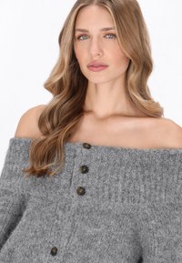Pulover gri, cu umerii descoperti, realizat dintr-un material tricotat texturat, având decolteu ribat și patru nasturi închiși la culoare pe față.