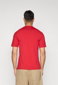 Rdeča majica s kratkimi rokavi iz bombaža, z okroglim izrezom in enostavnim dizajnom. Hrbet je gladek, brez vidnih logotipov ali vzorcev.