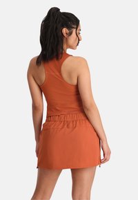 Sportieve oranje outfit met een mouwloos topje met een aansluitend ontwerp en een bijpassende rok met een elastische tailleband en zijritsen.