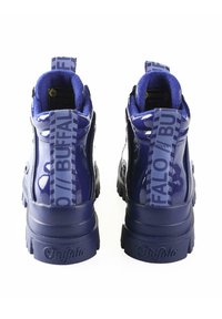 Botines de charol azul marino con cremalleras visibles, cuellos acolchados y etiquetas de logo en los tacones; suelas texturizadas para mayor agarre.