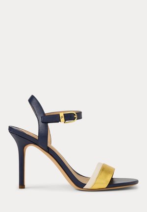 Granatowa sandałka na wysokim obcasie z złotą klamrą przy kostce, beżowo-złotymi paskami z przodu i cienkim obcasem typu szpilka na białym tle.