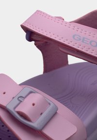 Κοντινή λήψη ροζ και μωβ σανδαλιού με ρυθμιζόμενους ιμάντες με γκρι πόρπη και απαλό, υφασμάτινο πέλμα.