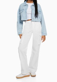 Ljusblå cropped denimjacka med rå kant och silvriga detaljer, tillsammans med vita vida cargobyxor som har sidofickor. Vita sneakers fulländar outfiten.