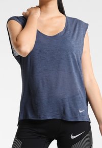 Námorně modrá sportovní tílko s krátkým rukávem, kulatým výstřihem, lehkou texturou a reflexním logem Nike v pravém dolním rohu.