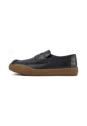 Mocasín de cuero negro con punta redondeada y suela marrón texturizada, mostrado en vista lateral sobre un fondo blanco.