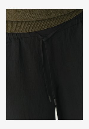 Črne hlače s elastiko in vrvico, izdelane iz teksturirane tkanine, z ohlapnim krojem, elastičnim pasom in nastavljivimi vezicami s črnimi plastičnimi konicami.