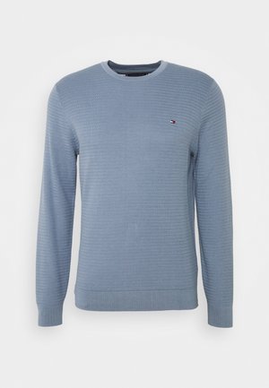 Maglione azzurro chiaro lavorato a maglia con trama a coste, scollo girocollo e maniche lunghe. Presenta un piccolo logo sul petto a sinistra.