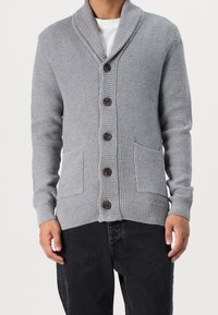 Grå stickad cardigan med en sjalkrage, fem bruna knappar och två framfickor med ribbade muddar och fåll.