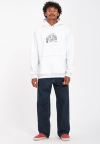 Grijze hoodie met voren een zak, met een kleurrijk grafisch ontwerp. Gecombineerd met donkerblauwe losse jeans en rode instap schoenen.