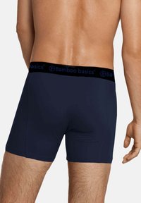 Marineblauwe bamboe boxershorts met een zwarte elastische tailleband, voorzien van "Bamboo basics" in blauwe letters, een gladde textuur en een aansluitend ontwerp.