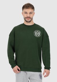Felpa verde con collo tondo e maniche lunghe. Presenta una stampa del logo sul davanti. Tessuto morbido con una vestibilità comoda e polsini a coste.