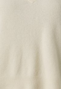 Kremkrāsas V-veida svītru džemperis, izgatavots no mīksta materiāla ar gludu tekstūru un ribotu apakšmalu. Vienkāršs dizains bez redzamiem rakstiem vai akcentiem.