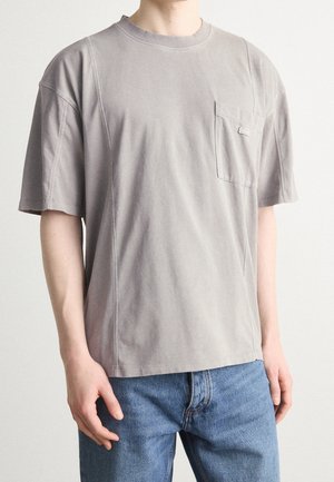 Grijze katoenen T-shirt met korte mouwen, ronde hals en een borstzakje. Heeft een comfortabele pasvorm en opvallende stikaccenten.