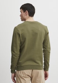 Hanorac verde cu mâneci lungi, guler rotund, manșete și tiv cu elastic. Fabricat dintr-un material neted și moale. Design simplu, fără logo-uri sau modele vizibile.
