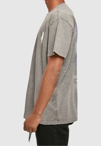 Grå bomulds t-shirt med løs pasform, korte ærmer og rund halsudskæring. Har et subtilt grafisk design på ryggen og tekstureret stof.