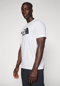 Hvit bomulls T-skjorte med en svart logo "The North Face" på forsiden, kortermet og klassisk rund hals.