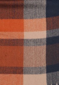 Tkanina w kratę z mieszanki wełny, prezentująca pomarańczowe, beżowe, granatowe i szare kwadraty, o miękkiej fakturze i skośnym wzorze jodełki.