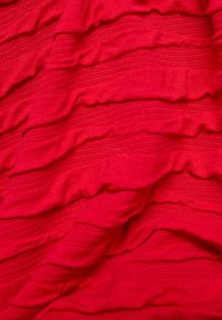 Roter Stoff mit horizontalen, strukturierten Rillen und Falten, die ein weiches, geschichtetes Muster erzeugen.