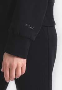 Czarna bluza z prążkowanymi mankietami, z małym, jasnym napisem na rękawie "To love!" Gładka, teksturowana tkanina.