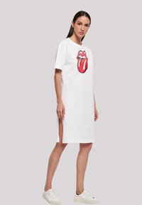 Weißes Baumwoll-T-Shirt-Kleid mit einem großen roten Zungen-Graphic auf der Vorderseite und seitlichen Schlitzen am Saum für zusätzlichen Komfort.