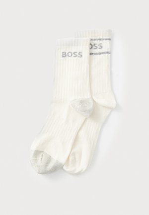 White ribbed socks with gray accents, featuring the word 'BOSS' on the cuff and a metallic gray toe. Soft material and medium length.