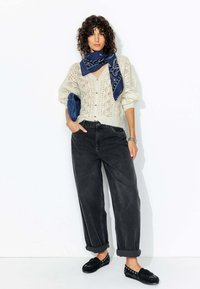Pull en maille torsadée crème avec des boutons, jeans larges gris foncé et mocassins noirs avec des accents en argent. Bandeau bleu noué autour du cou.