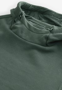 Sudadera verde oscura con cuello alto, que presenta un cordón y una textura suave. Tejido liso con detalles de costura mínimos.