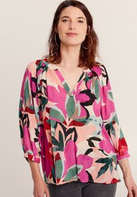 Blusa floreale colorata nei toni del rosa, rosso e verde. Presenta un colletto a V, maniche lunghe con dettagli arricciati e un tessuto leggero.