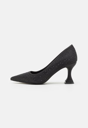 Black high-heeled shoe with a pointed toe, textured surface adorned with small black studs, and a distinctive flared heel design.