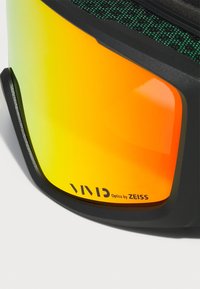Occhiali da sci neri con una grande lente arancione, dotati di una cinghia verde texturizzata e con il marchio "VIVID Optics by ZEISS".