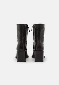 Bottes hautes jusqu'au genou en cuir noir avec un talon carré, présentant une texture lisse et une fermeture éclair à l'arrière pour un enfilage facile.