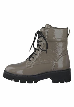 Botas de tobillo de charol beige con cordones negros, suela de goma gruesa y puntera redonda. Presentan una textura brillante y detalles de costura.