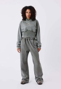 Grijze cropped hoodie en bijpassende brede broek gemaakt van zacht, textuur materiaal. Voorzien van een subtiele logo-accent en een trekkoord in de taille.