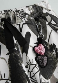 Bawełniane spodnie dresowe z czarno-białym abstrakcyjnym nadrukiem, elastyczną talią z czarnym sznurkiem oraz odpinanym brelokiem w kształcie serca ozdobionym cekinami.