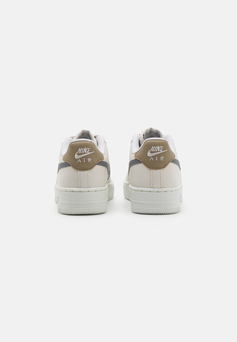 Sneakers Nike Air bianche con tomaia in pelle, dettagli grigi e beige, suola testurizzata e logo sulla parte posteriore.