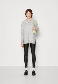 Svijetlosivi oversized pulover s bočnim prorezima, crne tajice od umjetne kože i crne loafers cipele. Dodatno je ukrašen malom zelenom torbicom preko ramena.