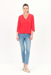 Rotes V-Ausschnitt-Oberteil mit Dreiviertelärmeln, kombiniert mit hellblauen, schmal geschnittenen Jeans und cremefarbenen, gestrickten Absatzsandaletten.