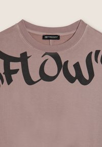 Sudadera de color rosa claro con escote redondo, presenta letras negras en negrita que deletrean "FLOW". Textura suave, diseño casual y ajuste relajado.