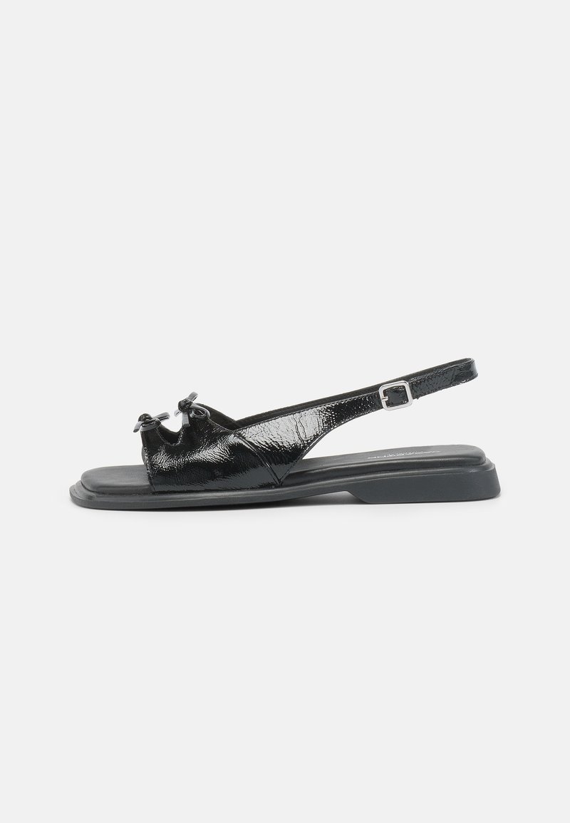 Sorte patenterte lær slingback sandal med flatt hæl, knute detaljer ved tåen og justerbar stropp. Jevn tekstur og minimalistisk design.