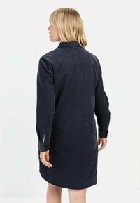 Czarna granatowa sukienka koszulowa wykonana z teksturowanej tkaniny; posiada kołnierz, długie rękawy zakończone guzikami oraz długość sięgającą do połowy uda.